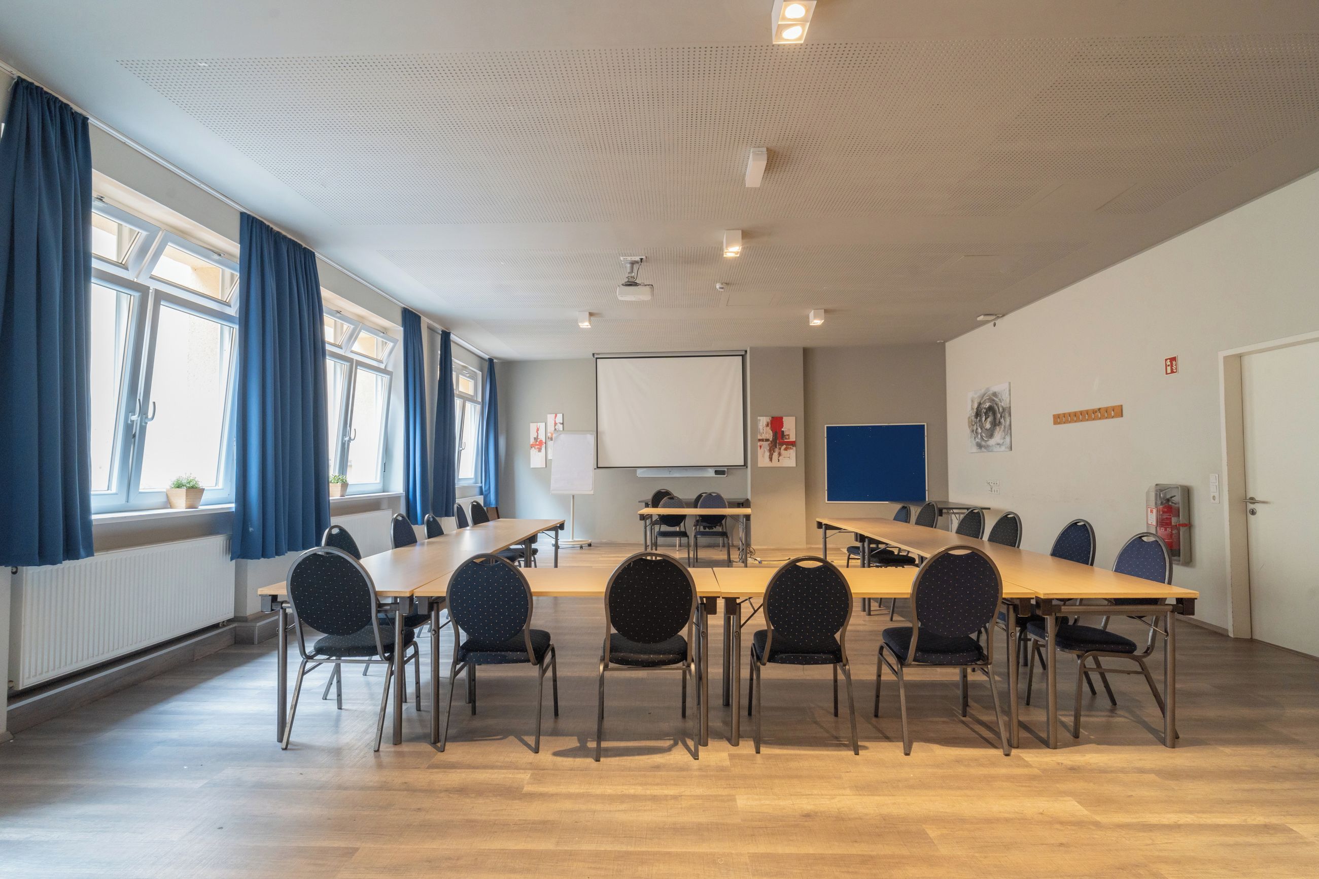 Ein Konferenzraum mit großem Tisch, Stühlen, einer Projektionsleinwand und einer Whiteboard-Tafel.