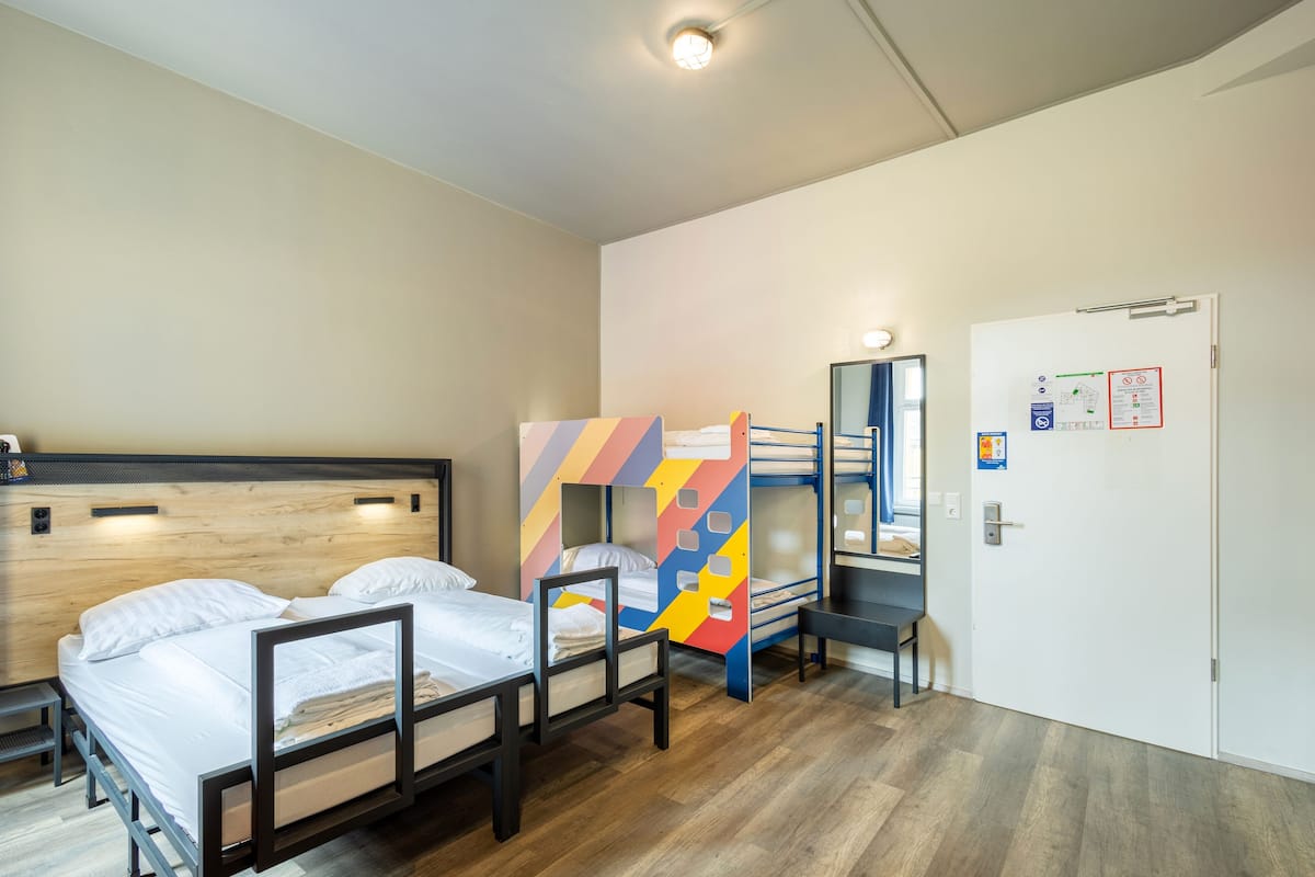 Une chambre de dortoir avec des lits superposés, un bureau et une porte sur laquelle est fixé un tableau d’affichage.