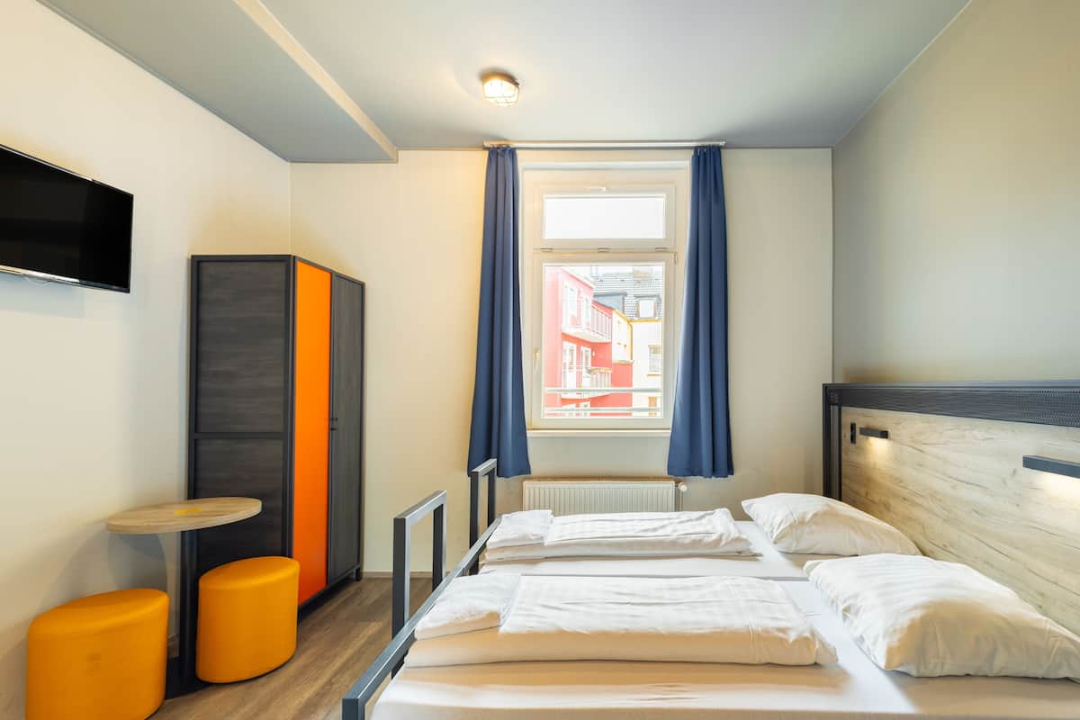 Une chambre d’hôtel avec un lit, une télévision, une petite table et deux tabourets orange.