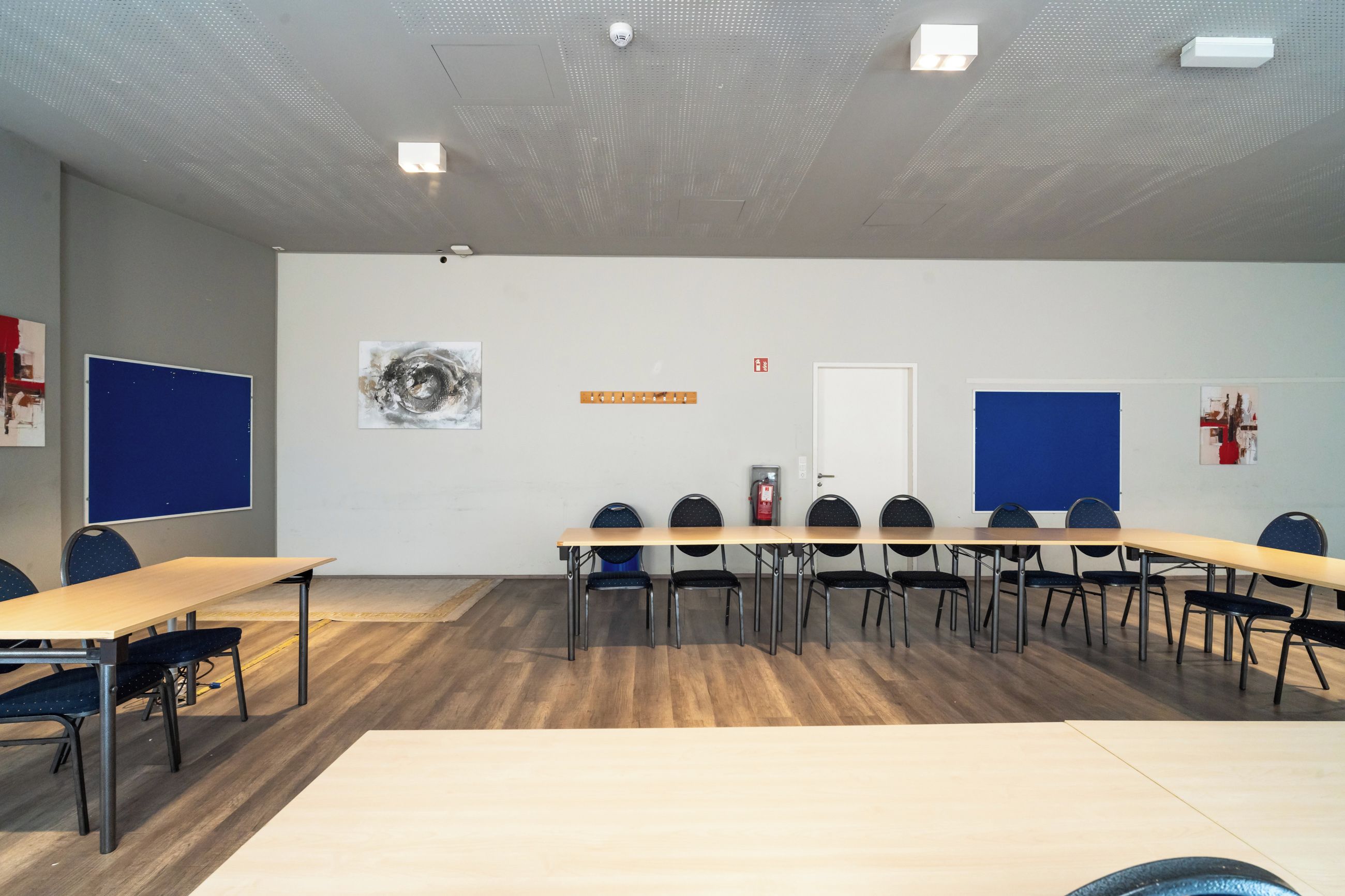 Sala de conferência com uma mesa comprida, cadeiras, quadro branco e extintor de incêndio.
