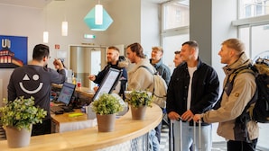 Een groep mensen bij een receptiebalie in een modern gebouw met grote ramen en potplanten.