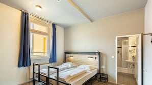 Een slaapkamer met een bed, een raam met gordijnen, een nachtkastje en uitzicht op de badkamer.