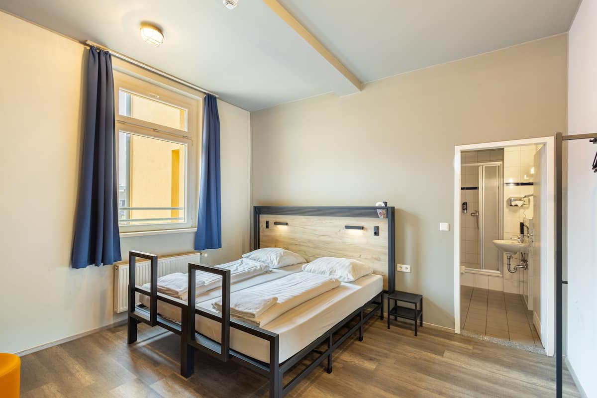 Une chambre à coucher avec un lit, une fenêtre avec des rideaux, une table de chevet et une vue sur la salle de bain.