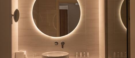 A modern bathroom with a round mirror, a sink, and a wooden vanity.
