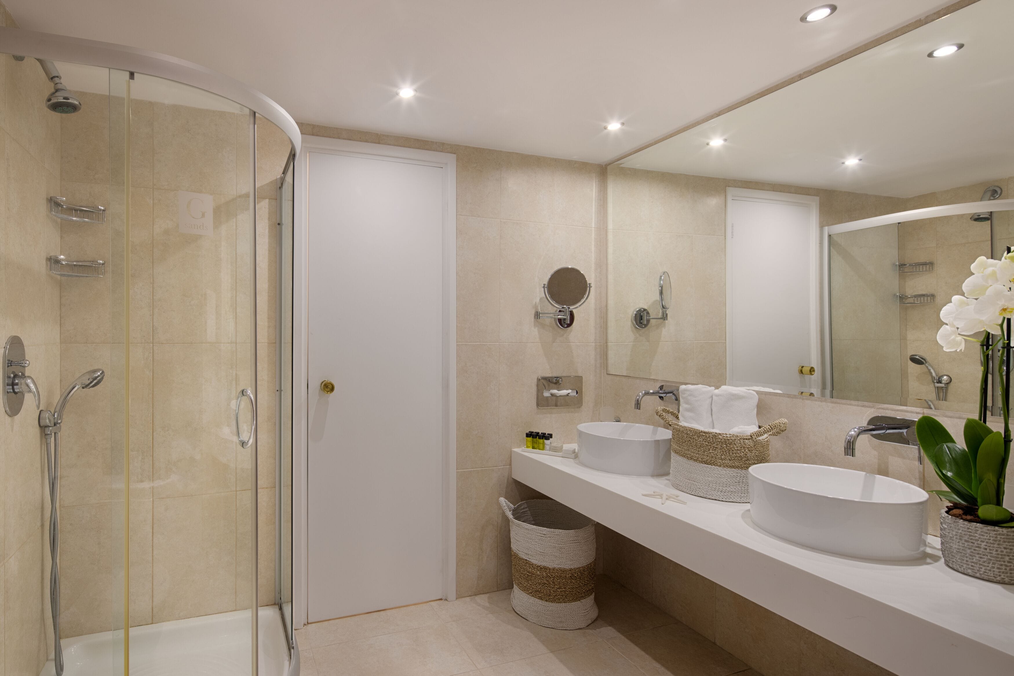 A modern bathroom with a glass-enclosed shower, a white sink with a large mirror, and a potted orchid.
