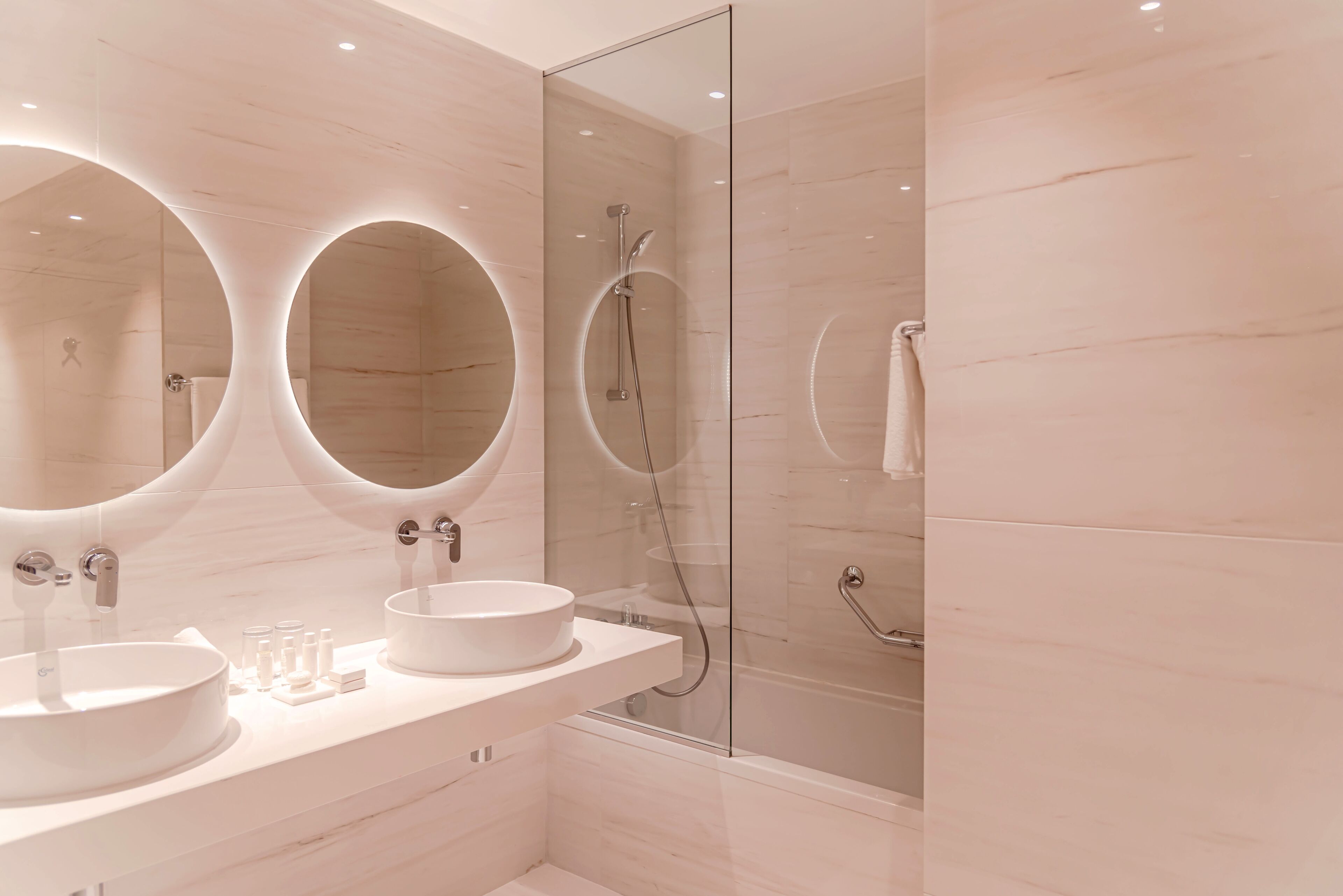 A modern bathroom with two round mirrors, a large sink, and a glass-enclosed shower.