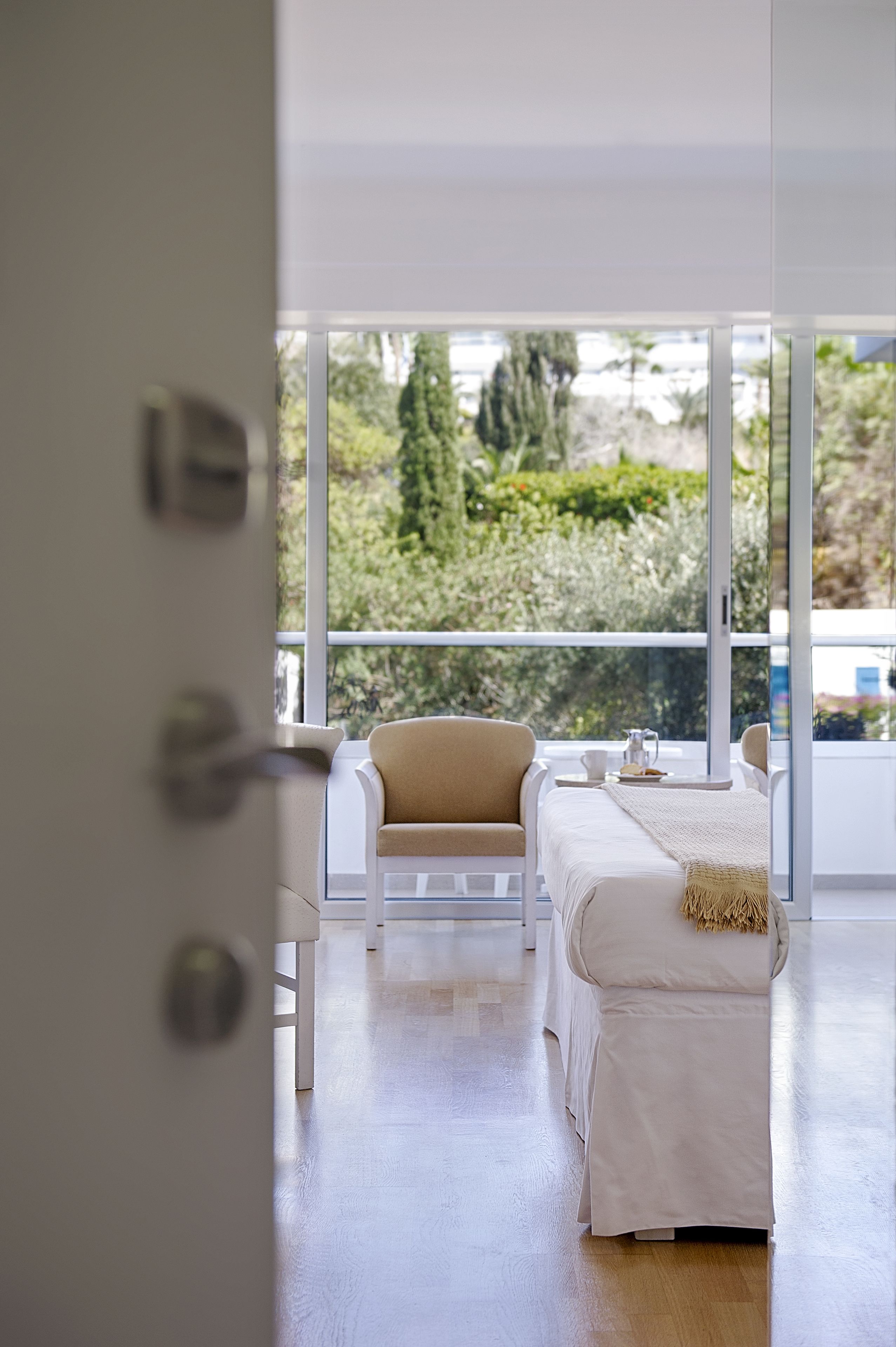 Een moderne slaapkamer met een groot raam, een bed, een stoel en een tafel met kop en schotel.