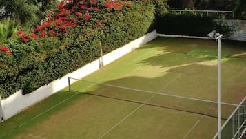 A tennis court with a net, surrounded by lush greenery and a view of the ocean.