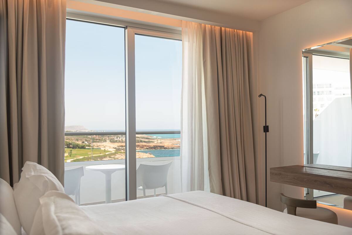 A hotel room with a large window, a bed, a bedside table, and a chair.