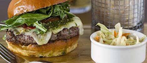 A burger with a bun, lettuce, cheese, and a toothpick. There is a basket of fries and a small bowl of coleslaw.