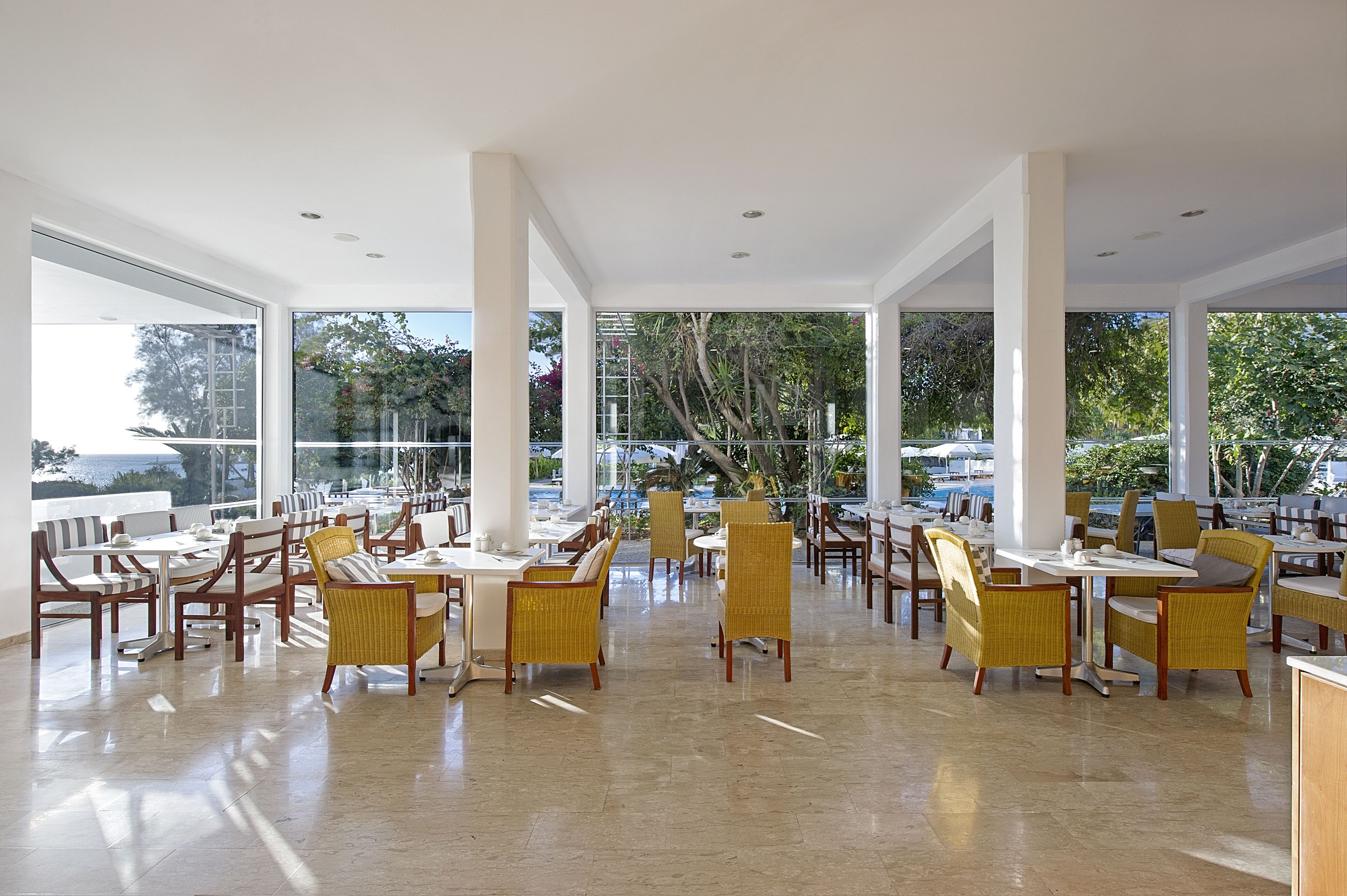 Un restaurant spacieux, doté de hauts plafonds et de grandes fenêtres offrant une vue sur la mer et les palmiers.