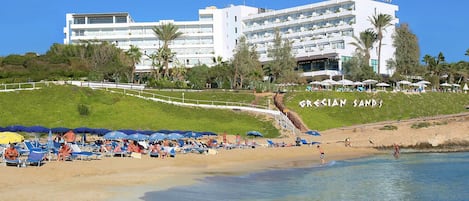 Ein Strandhotel mit mehreren Balkonen, einem Poolbereich und Strandsonnenschirmen.