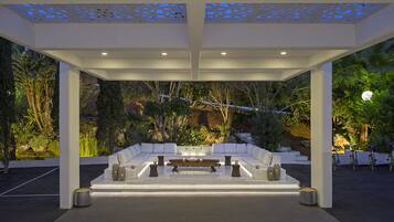 Un espace extérieur aménagé avec un canapé blanc et une table basse, entouré de plantes et d’arbres.