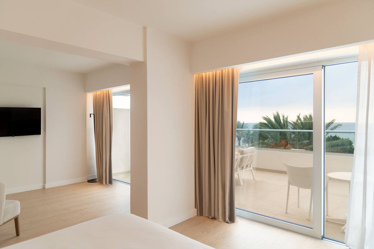 A modern hotel room with a large sliding glass door leading to a balcony with a view of the ocean.