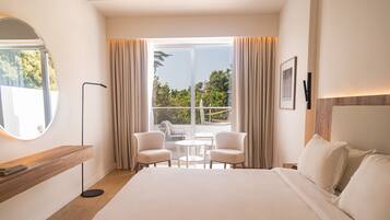 A hotel room with a large bed, a round mirror, a small table with two chairs, and a balcony with curtains.