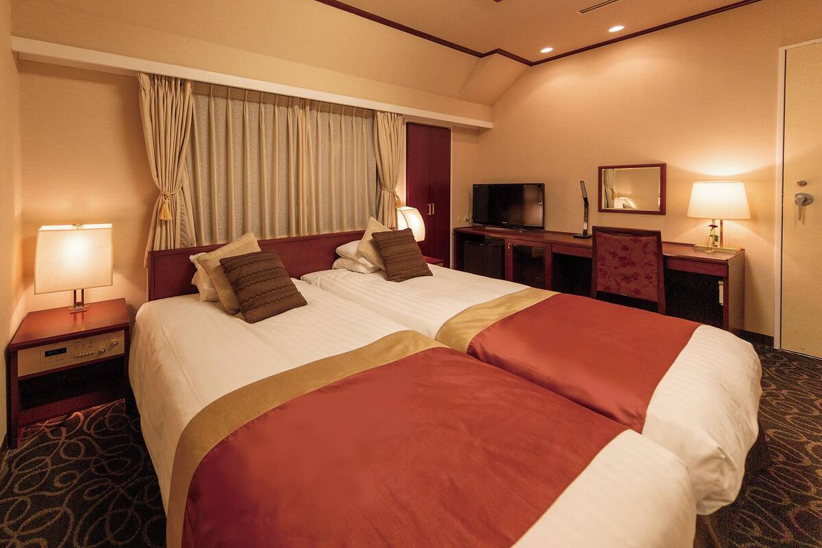 Una habitación de hotel con una cama grande, televisión, escritorio con lámpara y espejo.