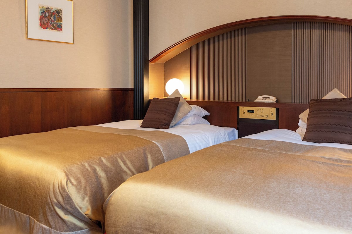 Habitación de hotel con dos camas, cabecero de madera, lámparas de noche y un teléfono.