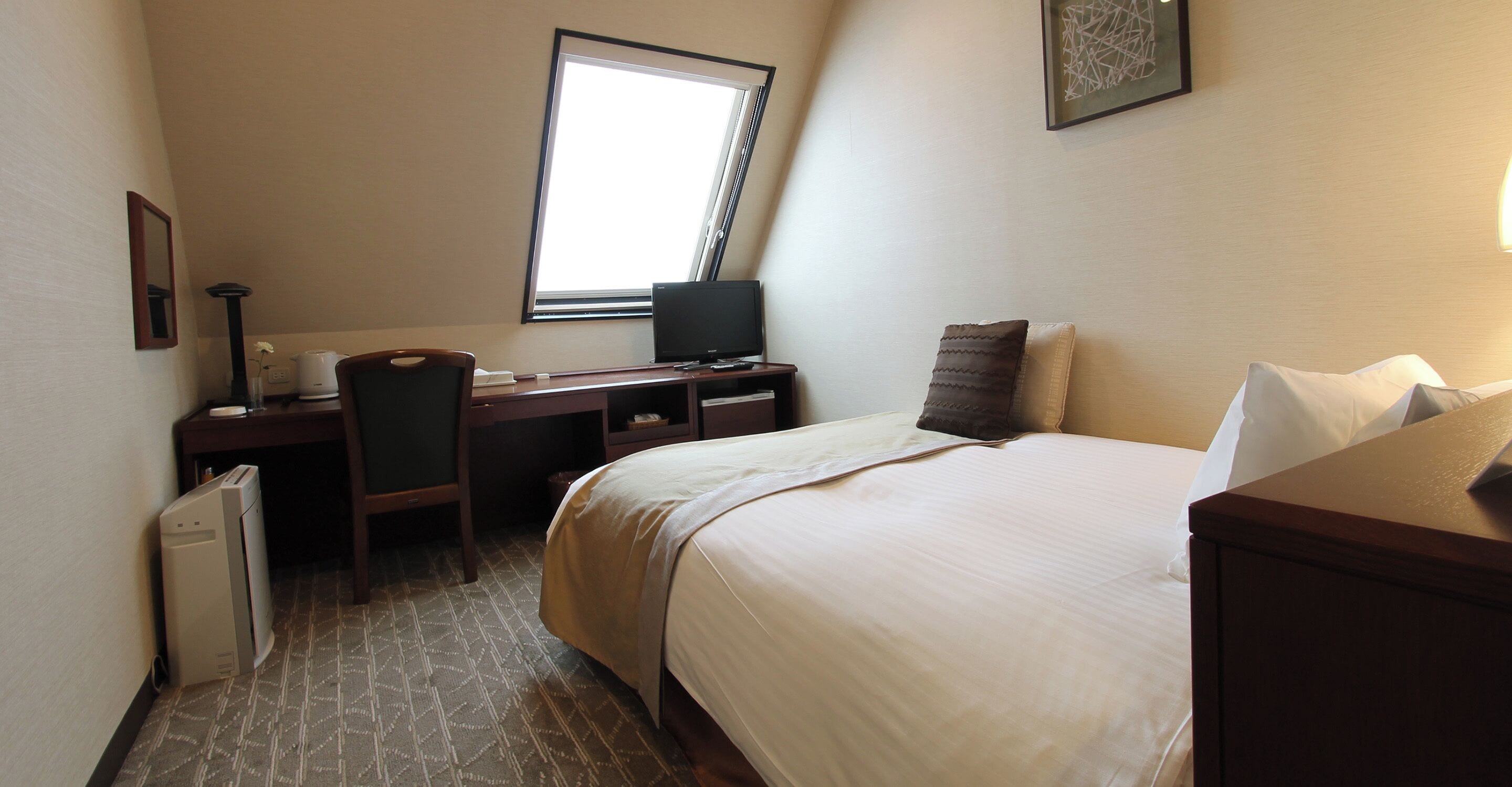 Une chambre d’hôtel avec un lit, un bureau, une chaise et une fenêtre.
