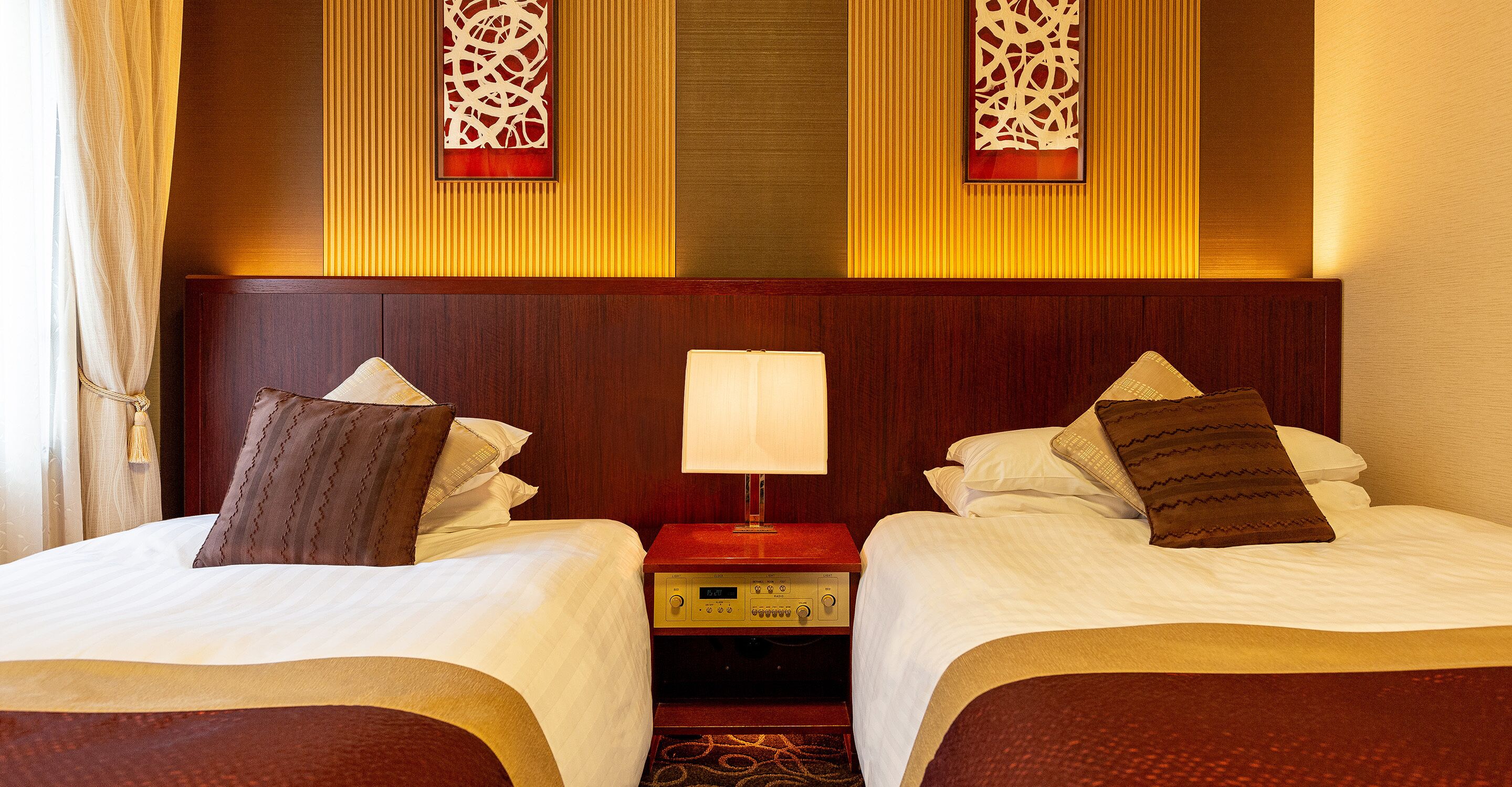 A hotel room with two beds, a nightstand with a lamp, and decorative wall panels.