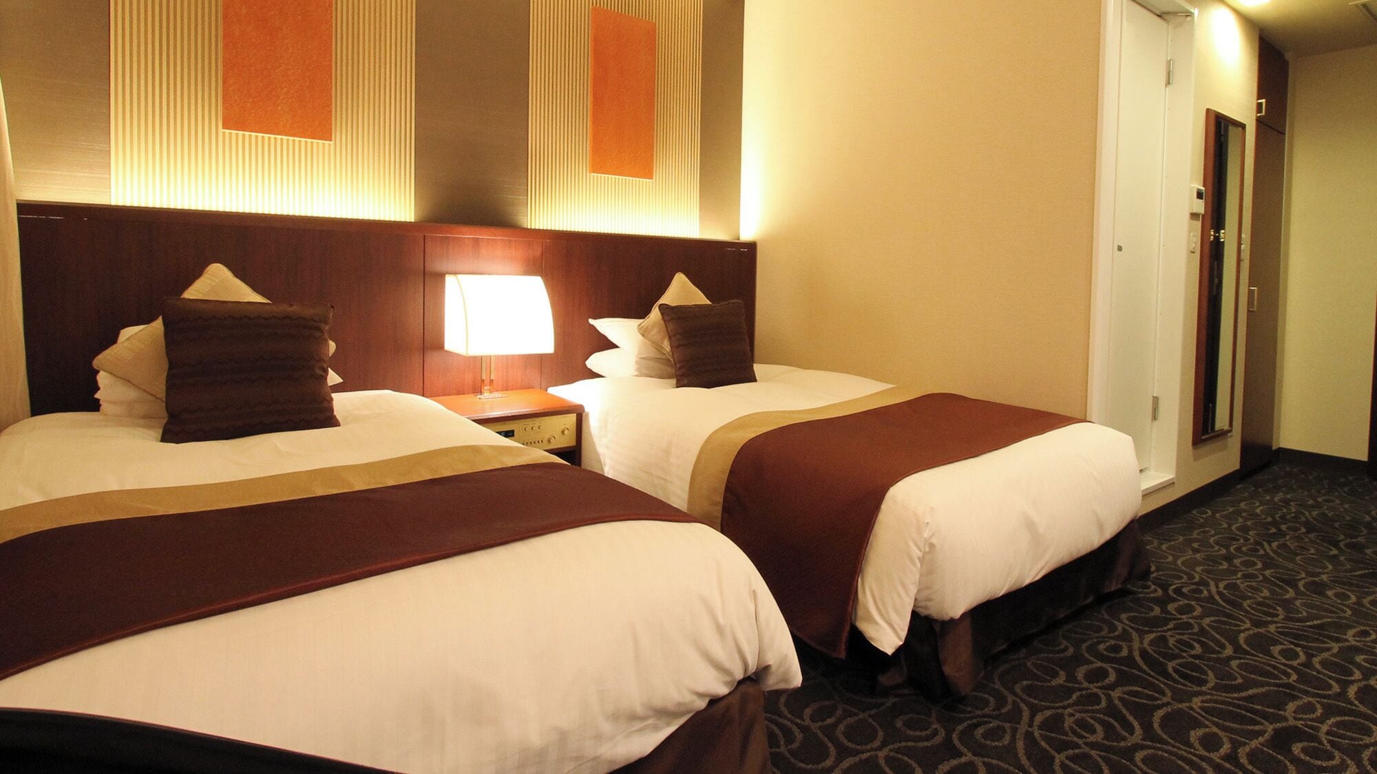 Dos camas de hotel juntas, con cabeceros, mesitas de noche con lámparas y suelo alfombrado.