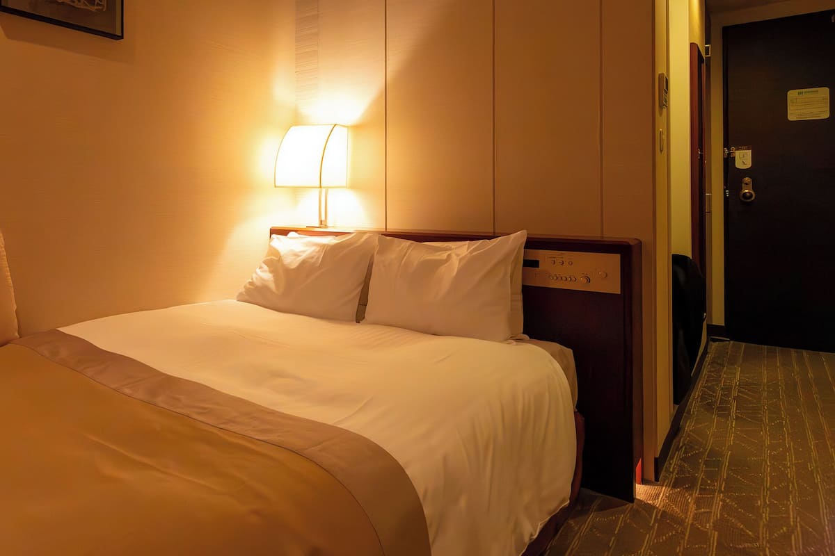 Una habitación de hotel con una cama, una mesita de noche, una lámpara y una puerta.