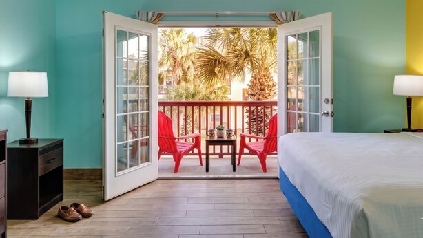 Een kamer met een bed, een tafel met stoelen en een balkon met rode stoelen en palmbomen.