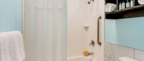 A bathroom with a shower, toilet, and a shelf with toiletries.