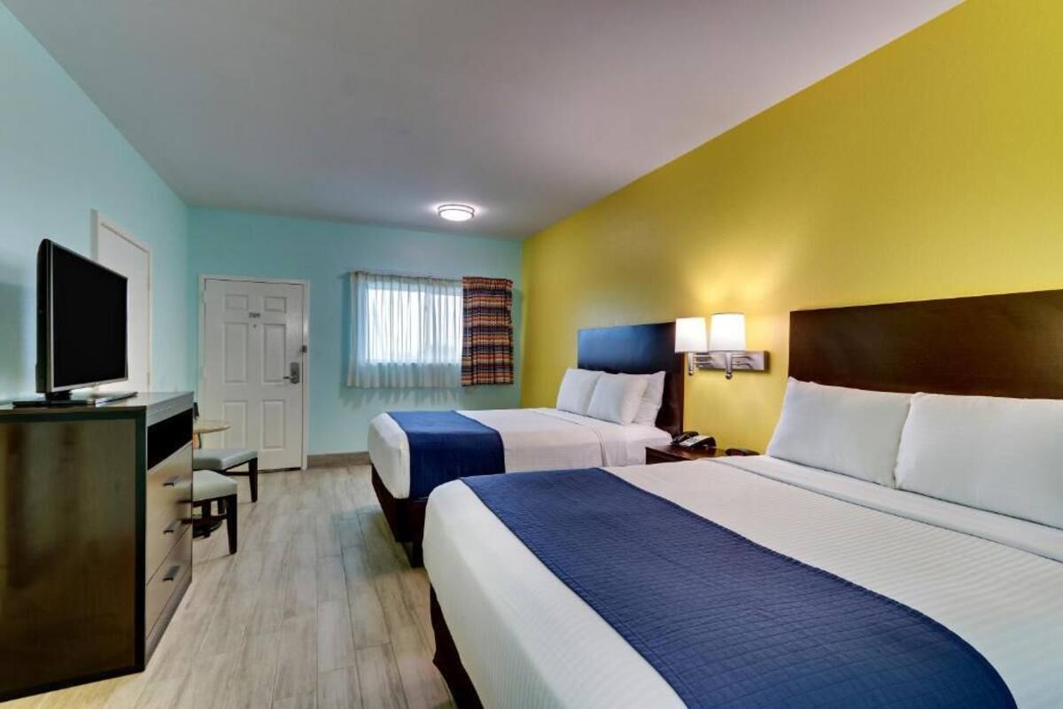 A hotel room with two beds, a desk, a television, and a window with curtains.