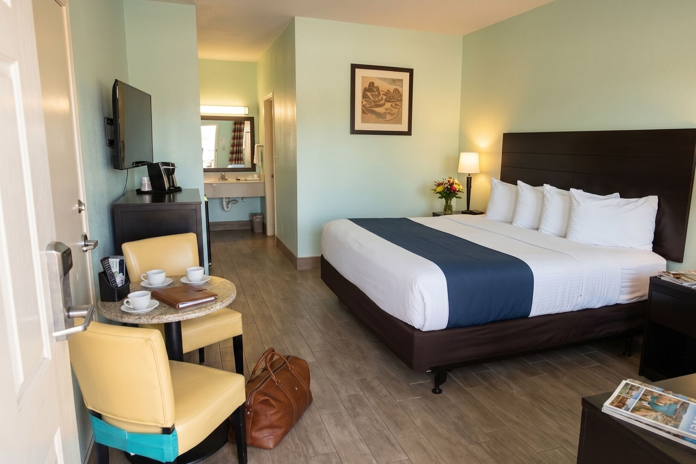A hotel room with a bed, a desk with a chair, a coffee maker, and a TV on the wall.