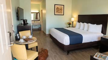 A hotel room with a bed, a desk with a chair, a coffee maker, and a TV on the wall.