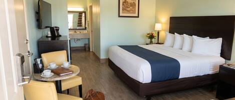 A hotel room with a bed, a desk with a chair, a coffee maker, and a TV on the wall.