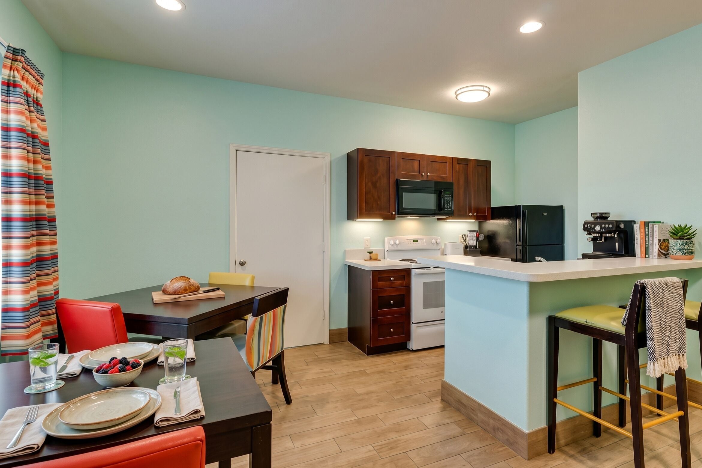 A compact kitchen with a microwave, oven, and refrigerator. There is a dining table with chairs and a small island with bar stools.