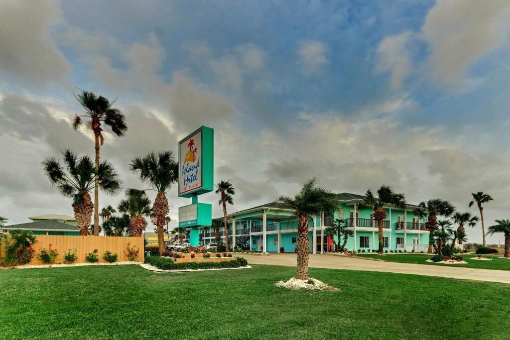 A hotel with a large sign, palm trees, and a blue building.