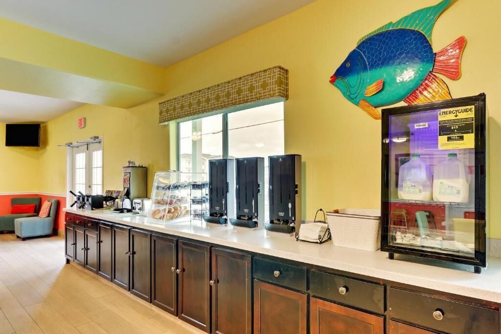 A reception area with a counter, a fish decoration, a refrigerator with a milk display, and a window with blinds.