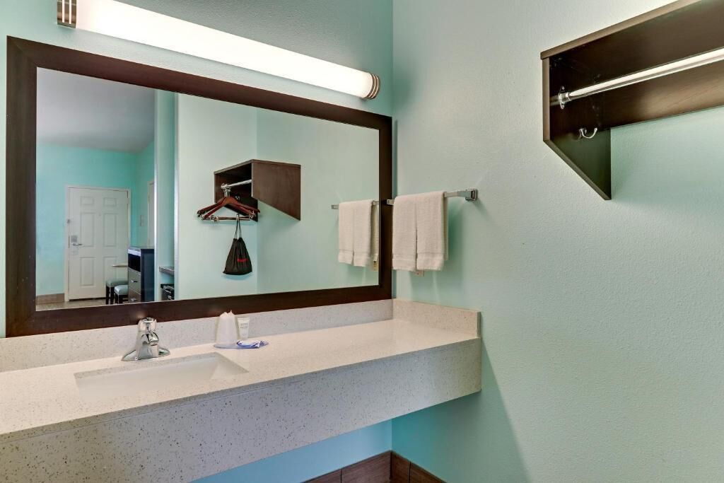 A bathroom with a large mirror, a sink, and a towel rack.