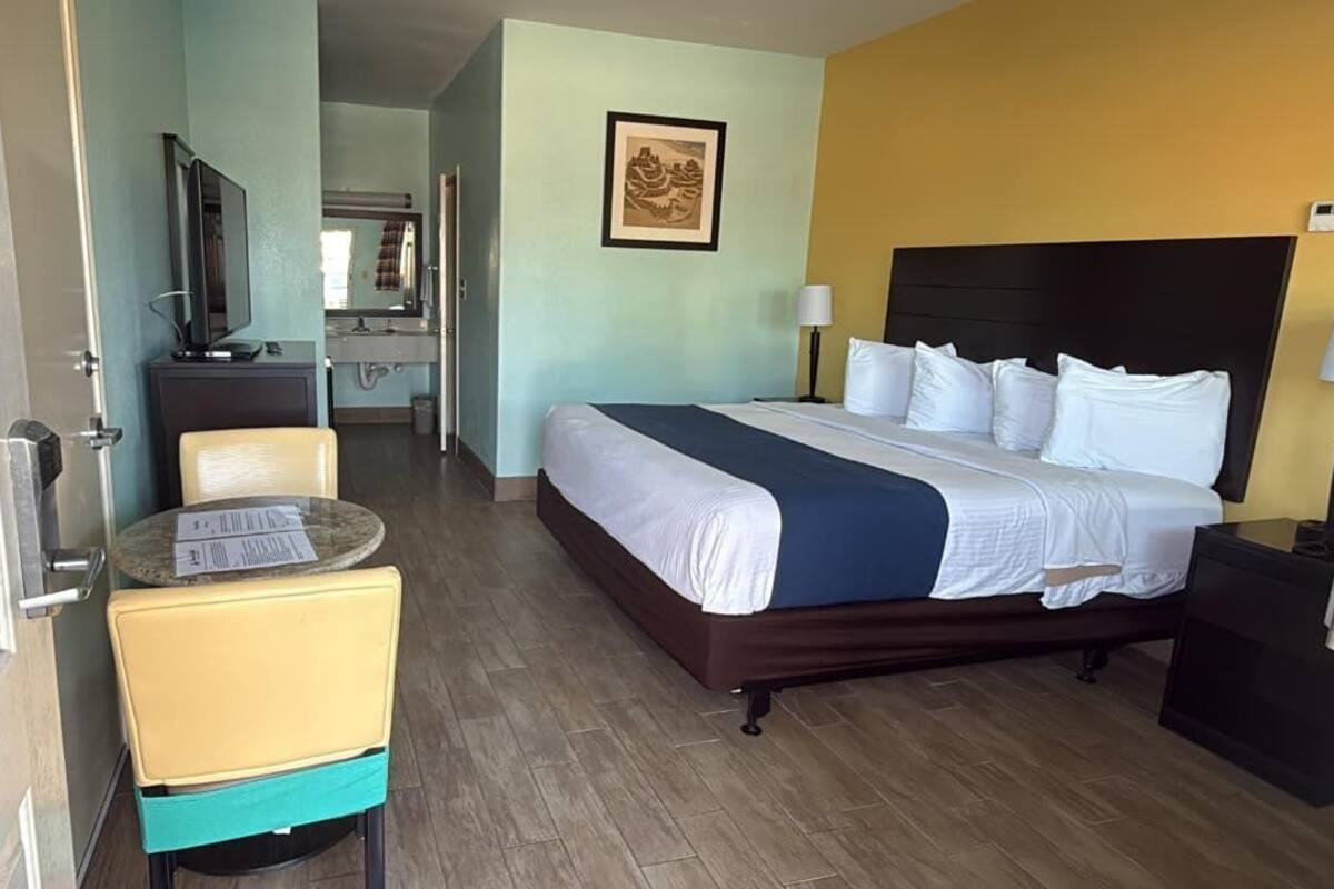 A hotel room with a bed, a desk with a chair, a television, and a bathroom visible in the background.