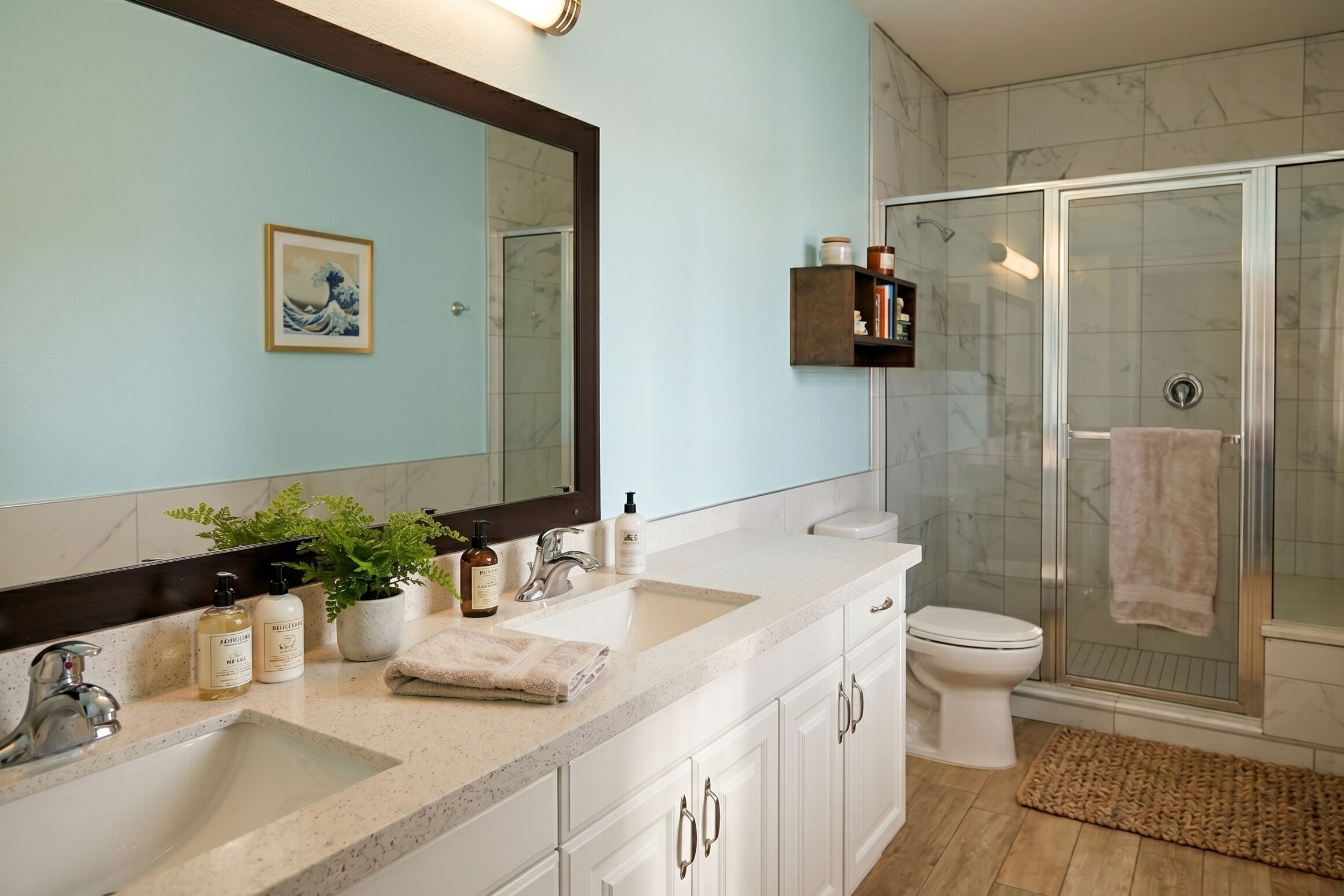 A bathroom with a large mirror, two sinks, a toilet, and a glass-enclosed shower.