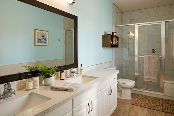 A bathroom with a large mirror, two sinks, a toilet, and a glass-enclosed shower. - The Island Hotel Near Beach Port Aransas (Port Aransas)
