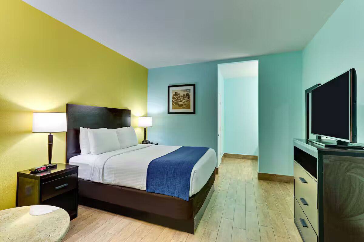 A hotel room with a bed, bedside tables, a TV, and a door leading to another room.