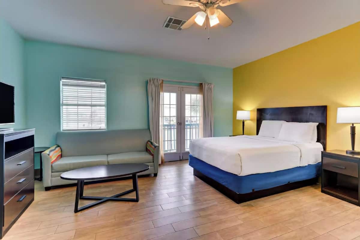 A hotel room with a bed, a sofa, a TV, a ceiling fan, and a window with curtains.