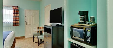 A compact room with a bed, a desk with a television, a microwave, and a coffee maker.
