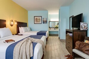 Ein Hotelzimmer mit zwei Betten, einem Fernseher, einem Schminktisch, einem Spiegel und einem Nachttisch mit Lampe.