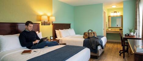 A hotel room with two beds, a desk, a chair, a lamp, and a mirror.
