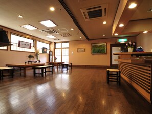 A spacious room with wooden flooring, multiple tables and benches, and a reception desk with a plant. - Nikko Sansui (Nikko)