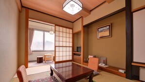 A traditional Japanese room with tatami flooring, a low wooden table, a cushioned bench, a television, and a painting on the wall. - Nikko Sansui (Nikko)