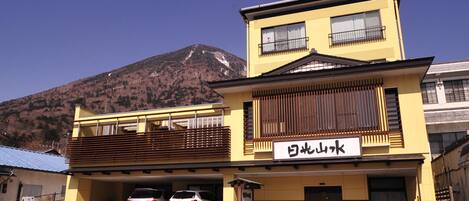 A two-story building with a yellow facade and a sign that reads "Yamato Mountain". There are two cars parked in front, and a mountain is visible in the background.