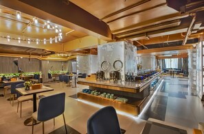 A modern hotel lobby with a central bar area, seating arrangements, and a decorative ceiling.