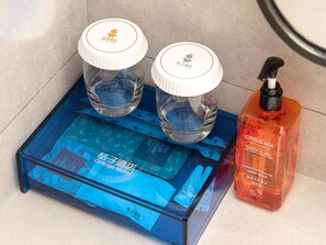 Two clear glass bottles with white lids and a red bottle with a black pump, placed on a blue tray with hotel branding. - Orange Hotel Guangzhou Quzhuang Metro Station (Guangzhou)