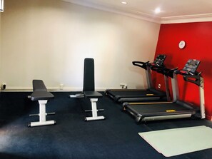 Une salle de sport équipée d’un banc, d’un banc de musculation et de deux tapis de course.