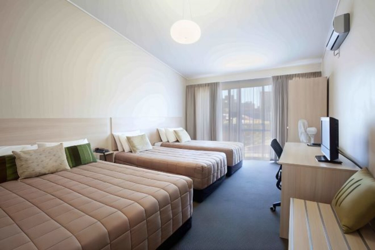 Une chambre d’hôtel avec trois lits, un bureau avec un ordinateur et une télévision.